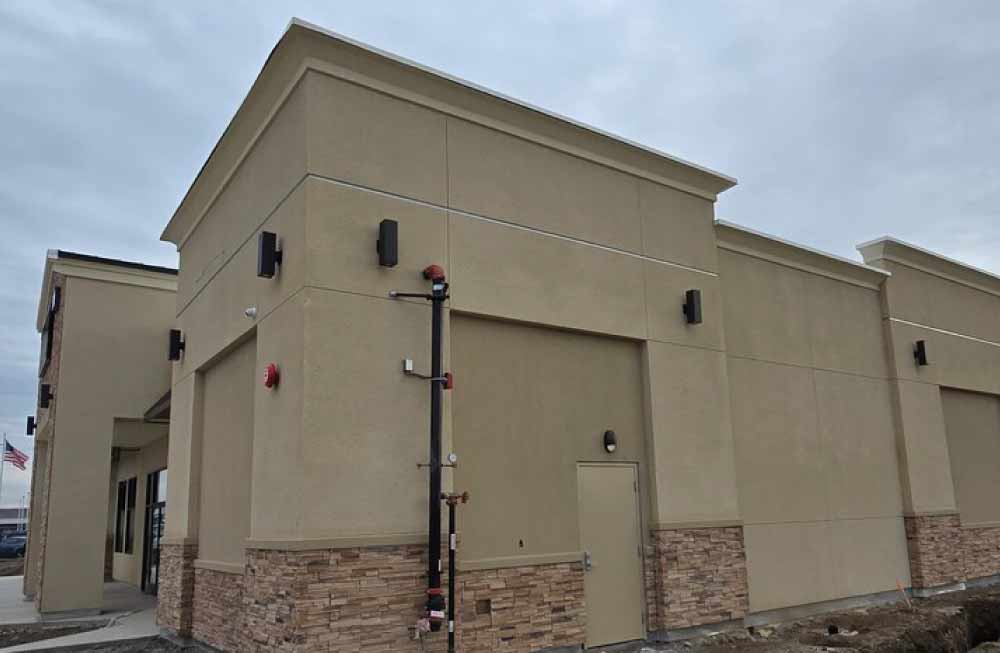 Side view of a finished commercial building showcasing a uniform sand-finish stucco application, clean expansion joints, and integrated stone veneer along the base.