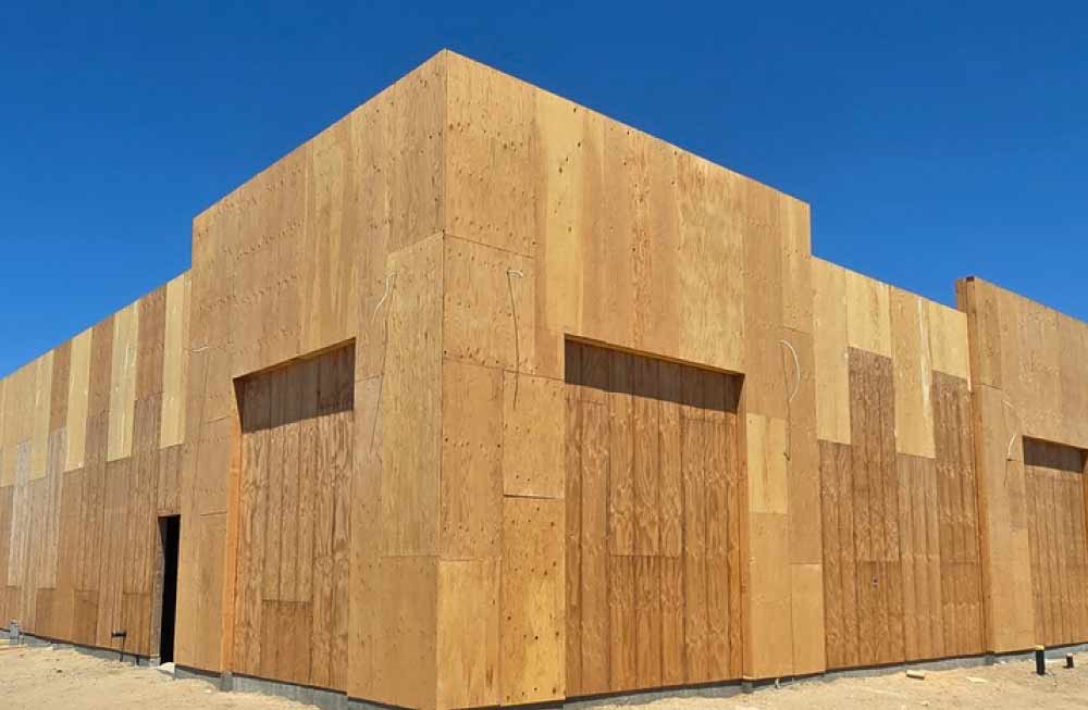 Corner perspective of a commercial building project showing extensive plywood substrate preparation before the application of durable, high-quality exterior stucco finishes.