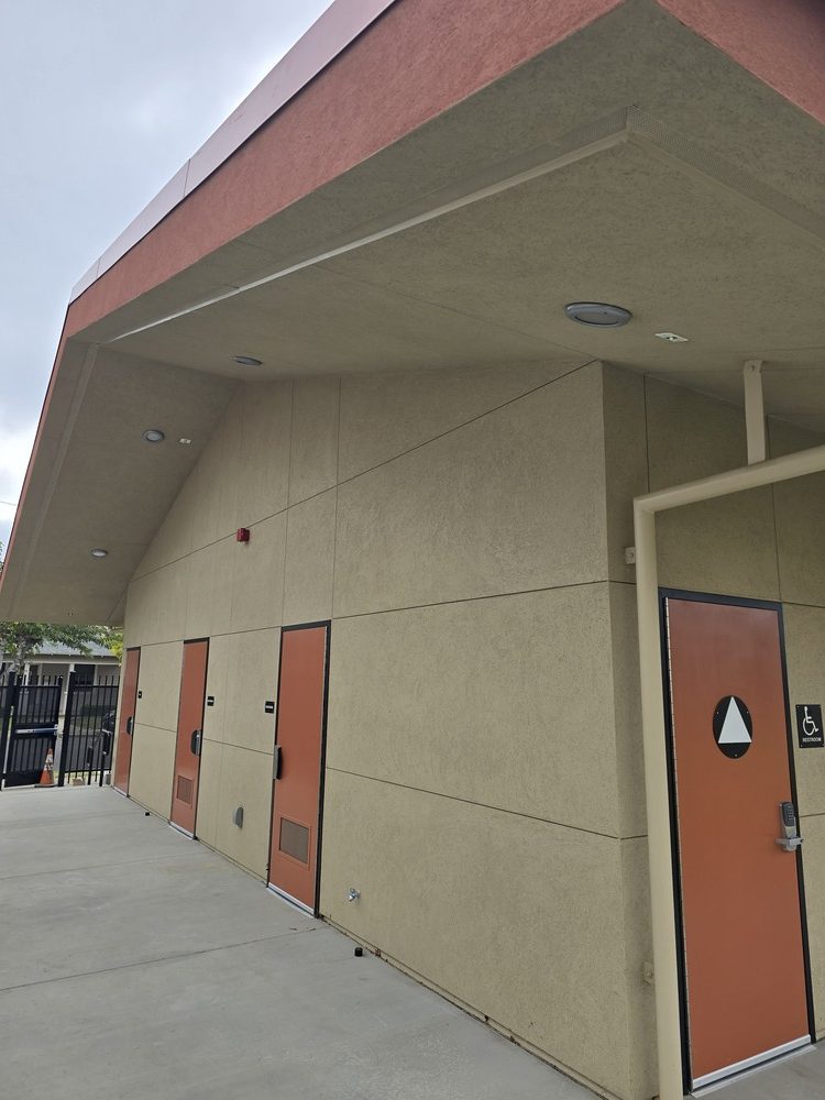 Textured tan stucco finish on a school building exterior featuring clean score lines and integrated metal door frames.