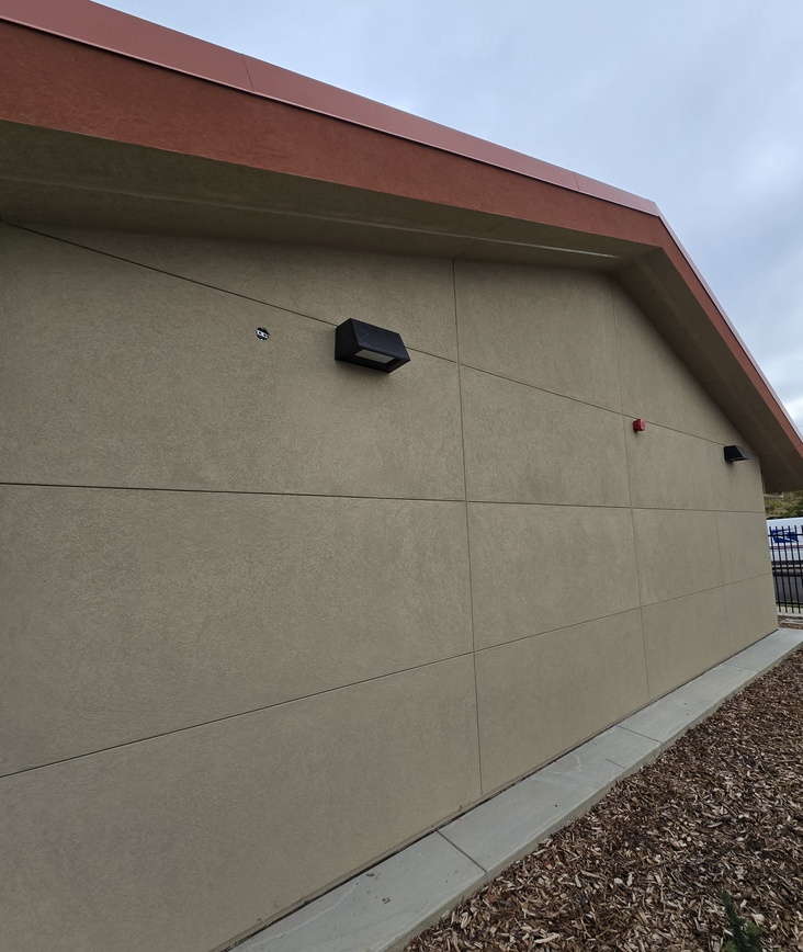 Expertly applied textured stucco on a school gable end showcasing a clean interface with the roofline and lighting fixtures.