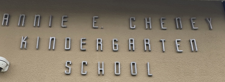 Close-up of a school nameplate mounted on a professionally textured sand-finish stucco wall at Annie E. Cheney Kindergarten.