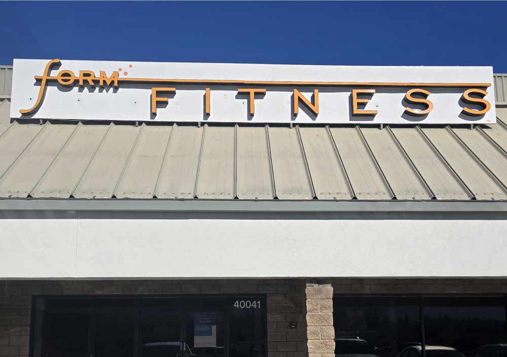 Expert commercial plastering work featuring a smooth white finish behind a Form Fitness business sign, demonstrating elevated brand identity through quality exterior finishes.