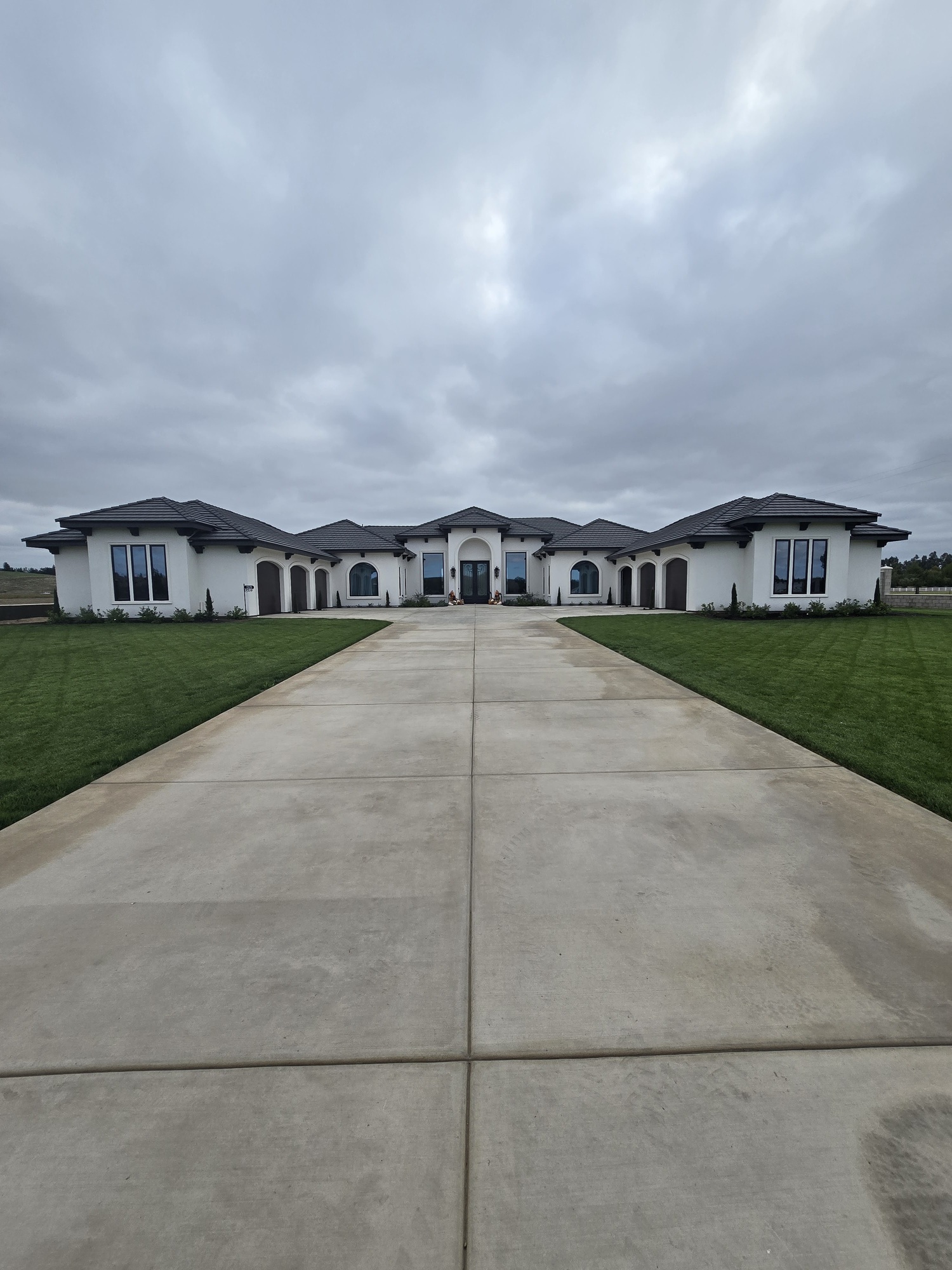 Perspective shot of a large residential estate with a long concrete driveway leading to a flawlessly applied white plaster facade and modern arched entryways.